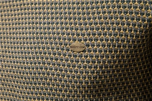 Detail der Hahnentritt-Strickstruktur mit ovalem AIOPESON Logo-Schild aus Metall