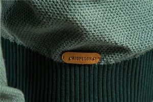 Detail of dark green honeycomb knit texture with branded leather logo tag on the hem