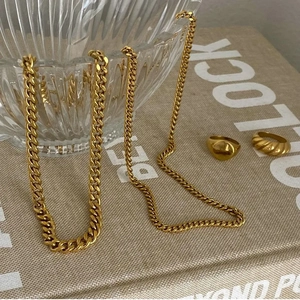 Detail shot of golden Cuban link chain necklaces and minimalist rings on a glass bowl