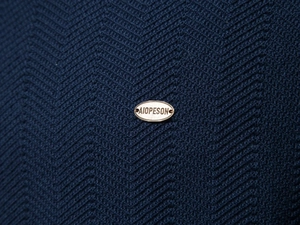 Macro shot of dark blue knit sweater showing herringbone pattern and metal logo
