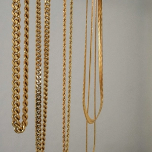 Detailed close-up of golden stainless steel Cuban, rope, and snake chains showing textures
