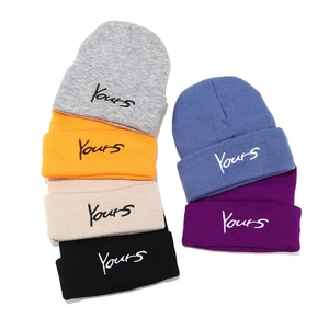Detail view of multicolored knitted beanies with Yours cursive letter embroidery