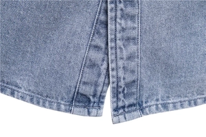 Détail de l'ourlet d'une veste en jean bleu clair avec double couture et fentes latérales