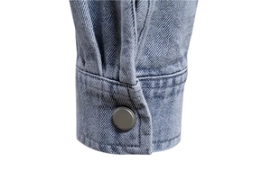 Détail du poignet d'une veste en jean bleu clair avec un bouton métallique argenté mat