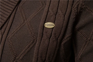 Detail shot of brown thick knit cardigan showing textured diamond cable patterns and metal logo