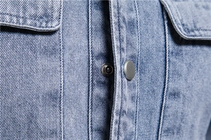 Détail de la patte de boutonnage en jean bleu délavé avec boutons-pression argent