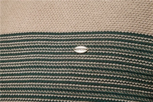 Gros plan du tissu en maille beige à rayures vertes avec plaque logo en métal AIOPESON