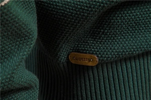 Détail macro du tricot vert foncé avec ourlet côtelé et écusson logo en cuir