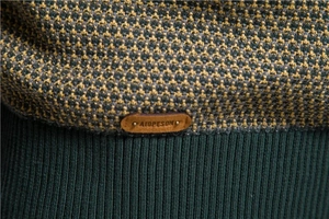 Detail der dunkelgrün-gelben Wabenstrickstruktur mit Marken-Patch aus Leder
