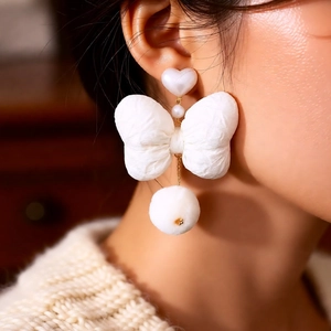 Close-up of pearl ribbon bow earrings with soft pom-pom drop on model side profile