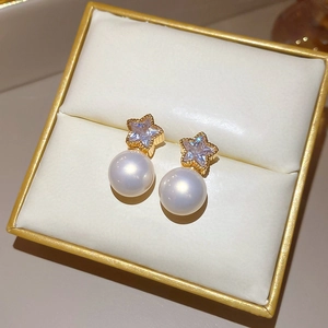 Detail of gold star earrings with sparkling zircon and white hanging pearls in a box
