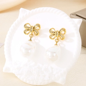 Detail of gold bow earrings with crystal pavé and baroque pearls on a white shell stand