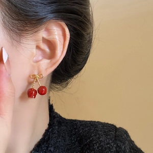 Detail of red cherry pendant earring with gold bow on model showing stylish texture