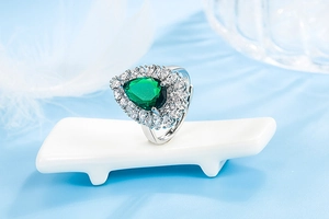 Macro detail of a teardrop emerald ring with micro-pave zircons on a white stand