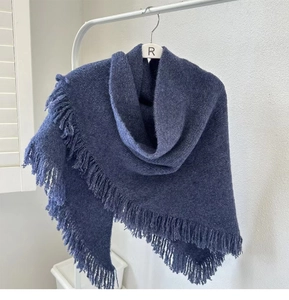 Detailed view of soft blue knitted shawl with elegant fringe hanging on a white wall