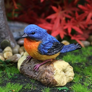 Realistic blue and orange resin bird ornament perched on a wood-textured garden base
