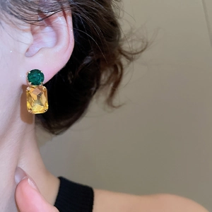 Detail of green and yellow square gemstone earrings shown on a model ear