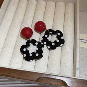 Close-up of red and black polka dot flower earrings displayed on a beige velvet jewelry box