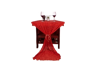 Detail of red wrinkled gauze table runner with hemp rope tie on dark wood table