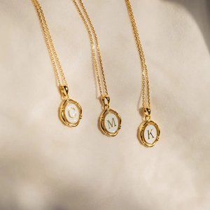 Golden personalized oval initial necklace with white enamel featuring letters C, M, K