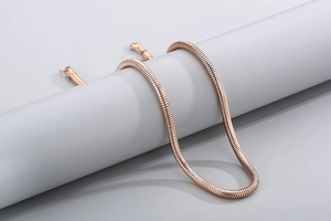 Détail de la chaîne serpent en or rose texturée drapée sur un support d'exposition gris