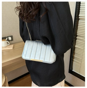 Detail of silver striped crossbody bag with golden chain strap and long metallic clasp