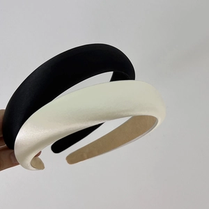 Detail view of thick satin headbands in black and ivory showing smooth glossy fabric