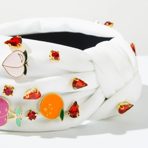 Detail of white knotted headband with colorful enamel fruit charms and red rhinestones