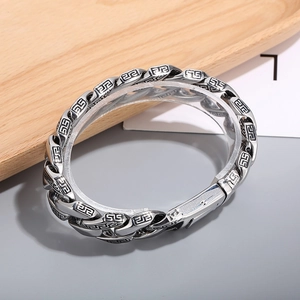 Detail of silver stainless steel Cuban chain bracelet with Greek key pattern carving