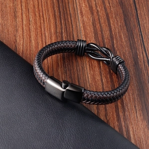 Detail of hand-woven black and brown leather bracelets with black metal clasp on wood surface