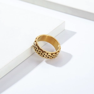 Detailed view of golden spinning ring with textured hollow cage design on white block