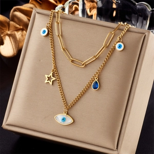 Detail of double-layer gold necklace featuring evil eye, star, and blue drop charms
