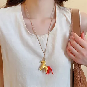 Minimalist golden horse pendant necklace with red bead tail on a beige cord