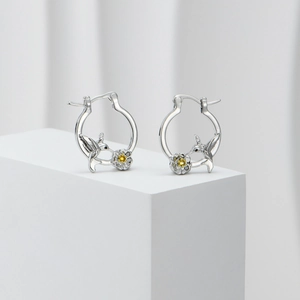 Detailed view of silver hummingbird earrings with yellow floral accents on white stand