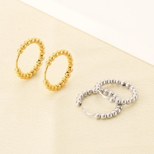 Detailed view of beaded hoop earrings in gold and silver finish on a neutral base