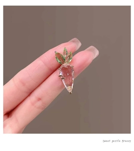 Macro shot of a pink crystal carrot brooch with green gems in a golden claw setting