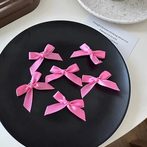 Close-up of six pink satin ribbon bows on a textured black plate with a coquette aesthetic