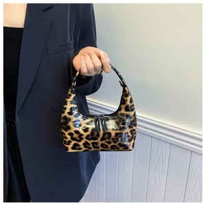 Close-up of patent leather leopard print hobo bag held by a model in a navy suit