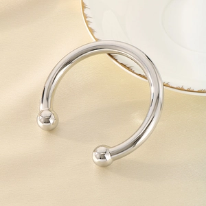 Close-up of a silver C-shaped open bangle with ball ends on champagne silk fabric