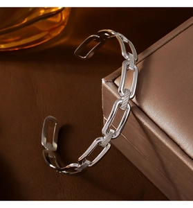 Gros plan d'un bracelet ouvert à maillons rectangulaires argentés sur un coffret doré