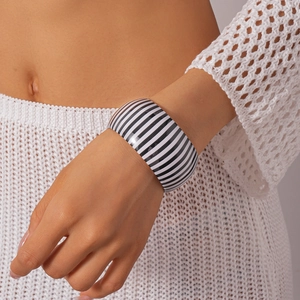Dettaglio di un ampio bracciale in acrilico a righe bianche e nere sul polso di una donna