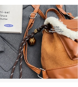 Detail of brown suede backpack featuring fuzzy trim and braided rope bell charm