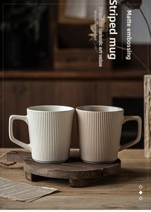 Detail of matte ceramic mugs with embossed stripes and unique square handles on wood