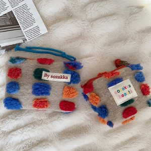 Detail of plush felt bucket bags with colorful pom-poms on soft white texture