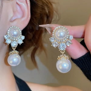 Close-up of elegant gold pearl drop earrings with sparkling diamonds on a model