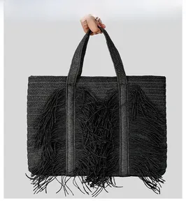 Detail of black woven straw tote bag with long bohemian fringe accents and dual handles