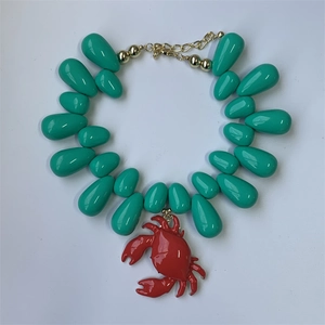 Close-up of green teardrop beads necklace with a red crab pendant and gold clasp