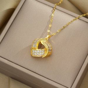 Detail shot of a gold geometric twisted pendant with clear zircons in a beige jewelry box