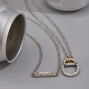 Detail of silver chain necklace featuring hammered texture pendants and gold accents