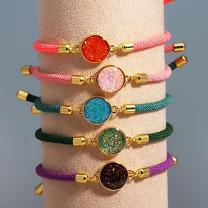 Detail view of colorful braided rope bracelets with glitter resin charms on a beige stand